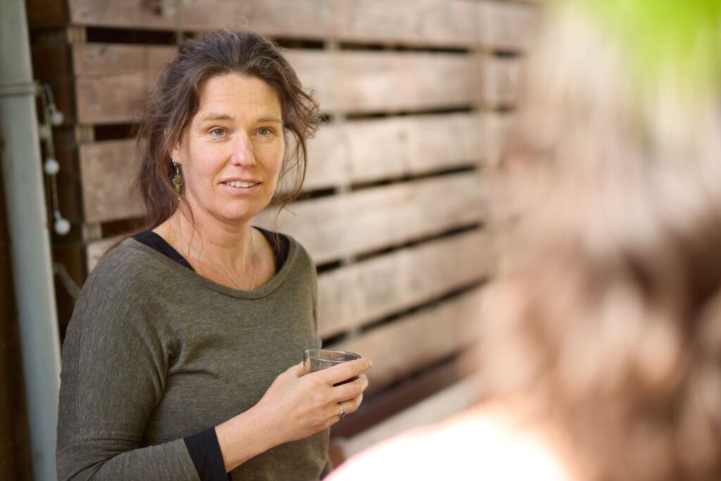 Ester heeft een kopje koffie vast en leunt tegen de schutting