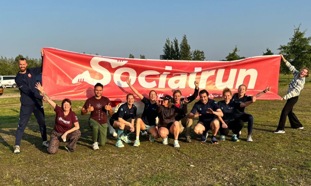 Team Tussenvoorziening knielt en houdt een grote Socialrun vlag omhoog bij de start