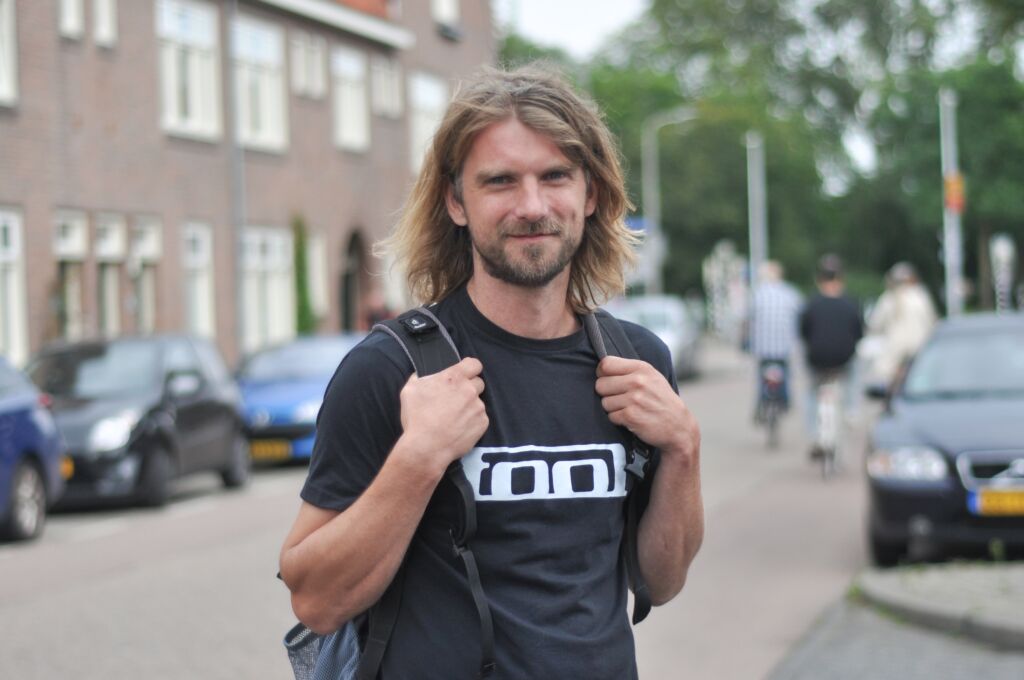 Luuk staat buiten op straat met zijn rugzak en kijkt met een lach naar de camera.