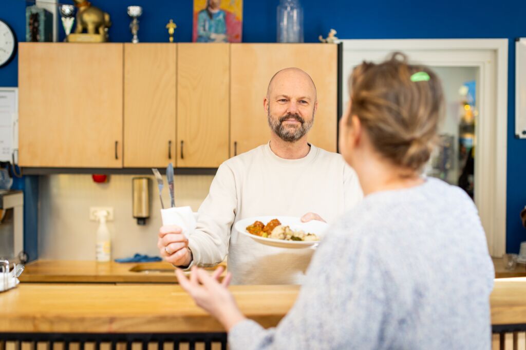 Jan-Peter geeft een bordje met eten aan een vrouw
